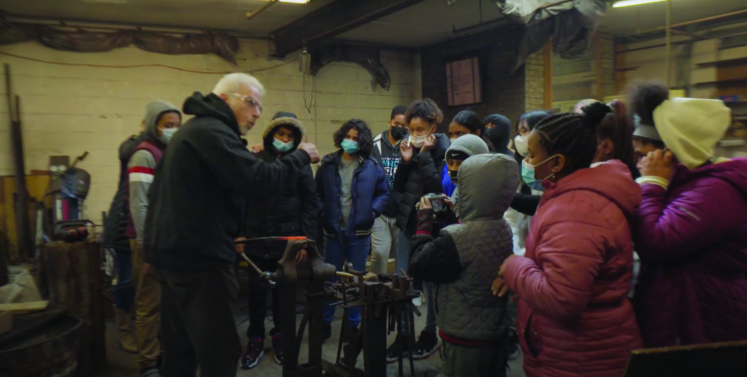 Group of students gathered around a blacksmith learning about legacy businesses.