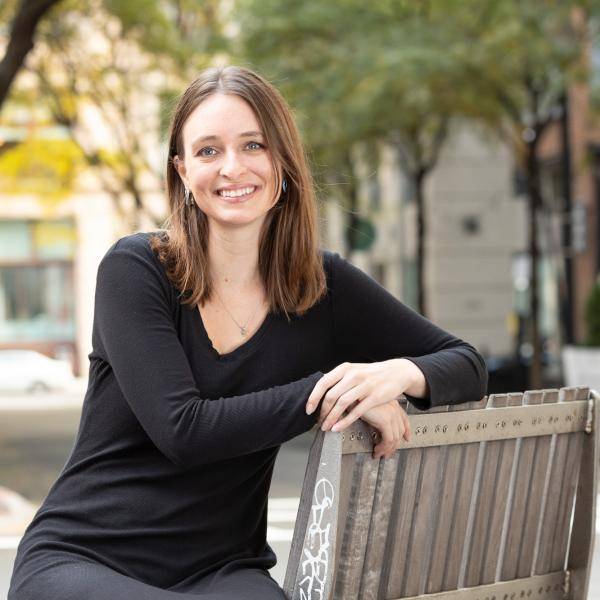 Amanda Malone is wearing a black dress and she is setting on a bench