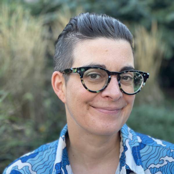 Thea is looking at the camera. She is using a blue shirt, glasses and she has a short haircut.