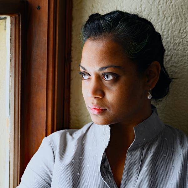 A portrait of Kali Noble standing next to a window with light washing across her face. 
