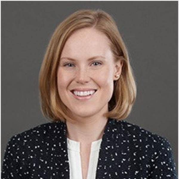 A photograph of Nancy Welsh smiling in front of a grey background. 